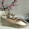 CUÑA DE ESPARTO CON PLATAFORMA Y DETALLE DE YUTE TRENZADO M.797-5 ORO 13 Cuña de esparto oro brillo tipo alpargata con puntera cerrada, hebilla y plataforma de yute