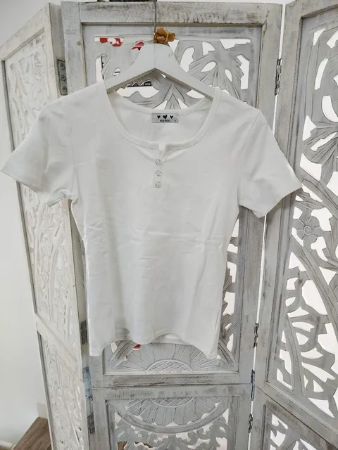 CAMISETA BLANCA CON DETALLES DE BOTONES M.CB/BO 1 Camiseta blanca con botones, manga corta y escote redondo con abertura central