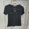 CAMISETA NEGRA CON FRUNCE Y DETALLE DECORATIVO M.YT-NEGRA 4 Camiseta negra con frunce frontal, escote en pico, manga corta y aplique decorativo