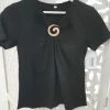 CAMISETA NEGRA CON BROCHE DORADO M.CM-NEGRA 6 Camiseta negra broche dorado con escote en pico, manga corta y aplique decorativo en el delantero