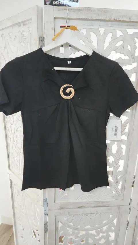 CAMISETA NEGRA CON BROCHE DORADO M.CM-NEGRA 1 Camiseta negra broche dorado con escote en pico, manga corta y aplique decorativo en el delantero