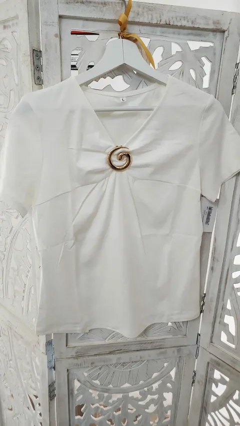 CAMISETA BLANCA CON BROCHE DORADO M.CM-BLANCA 1 Camiseta blanca broche dorado con escote en pico y manga corta en algodón con elastán