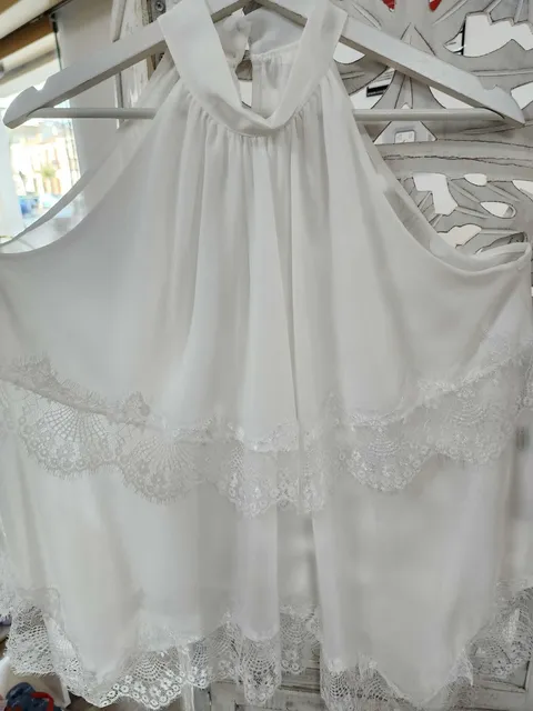 BLUSA BLANCA CON ENCAJE DE PUNTILLA FESTONEADO M.PUN/FES 1 Blusa blanca de puntilla festoneada, sin mangas y con cuello halter fruncido